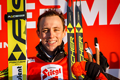 Das farbige Portrait zeigt einen strahlenden jungen Eric Frenzel mit Sprungski, Laufski und Stöcken in den Händen.